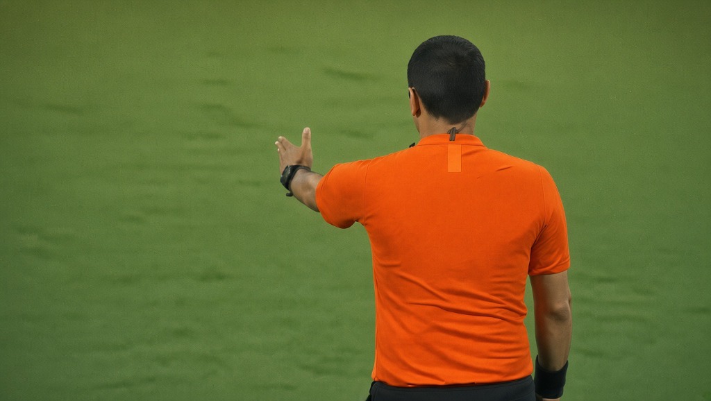 Football referee in orange shirt gesturing on the pitch